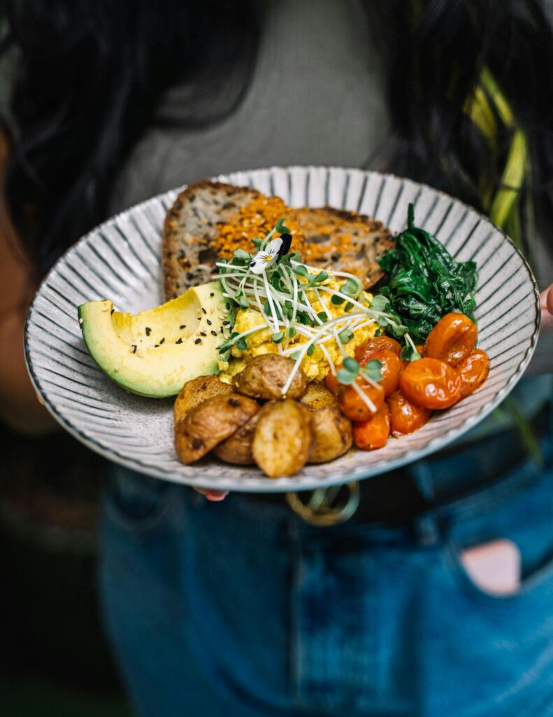 A colorful plate of avocado, potatoes, tomatoes, greens, and bread for a nutritious meal.